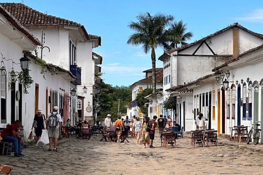 A cobblestone street lined with white buildings, palm trees, and outdoor seating areas. 5