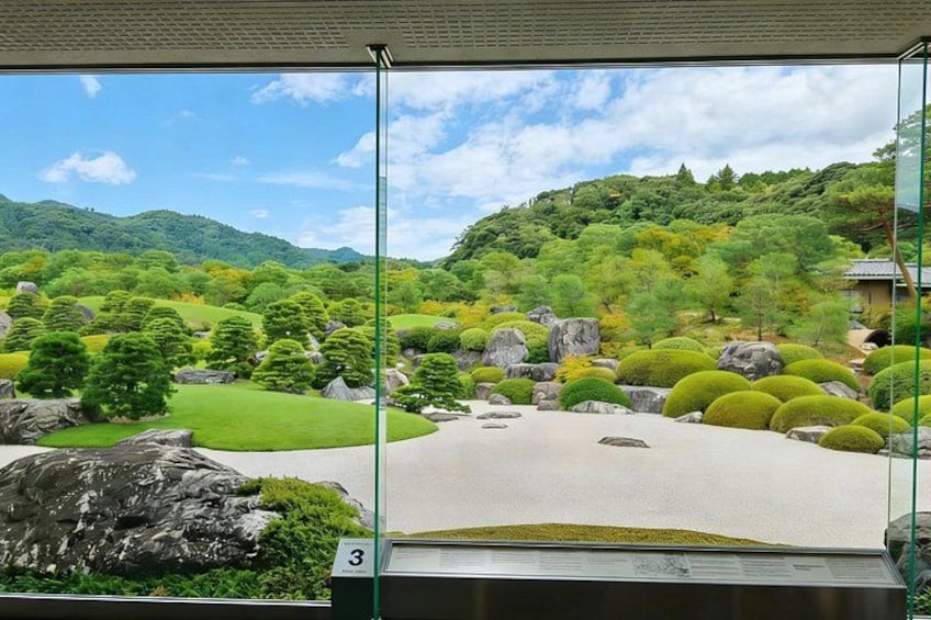 Un jardín japonés tradicional con vista a un paisaje montañoso a través de un ventanal. 2