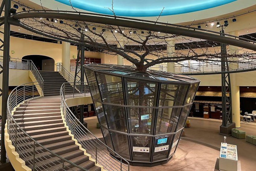 Un interior moderno con una escalera de caracol, un ascensor de vidrio y una escultura de árbol. 5