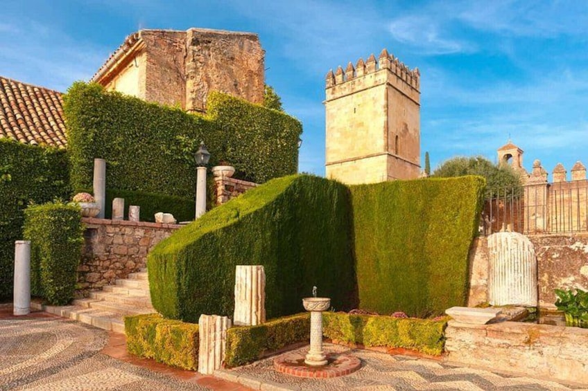 Un edificio histórico con una torre, un seto cuidado y un camino pavimentado. 2