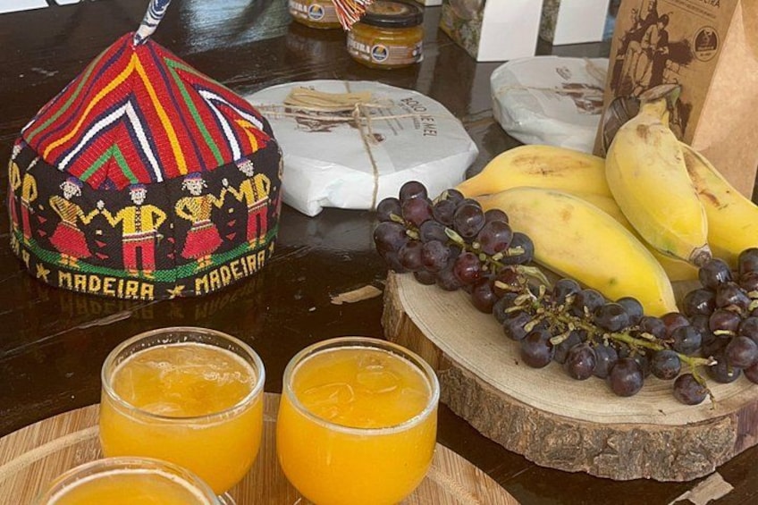 Ett bord med en färgglad hatt, ost, bananer, vindruvor och glas med apelsinjuice. 5