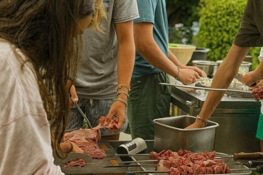 Des personnes préparent des aliments à l’extérieur, avec de la viande sur un gril et des ustensiles de cuisine à portée de main. 2