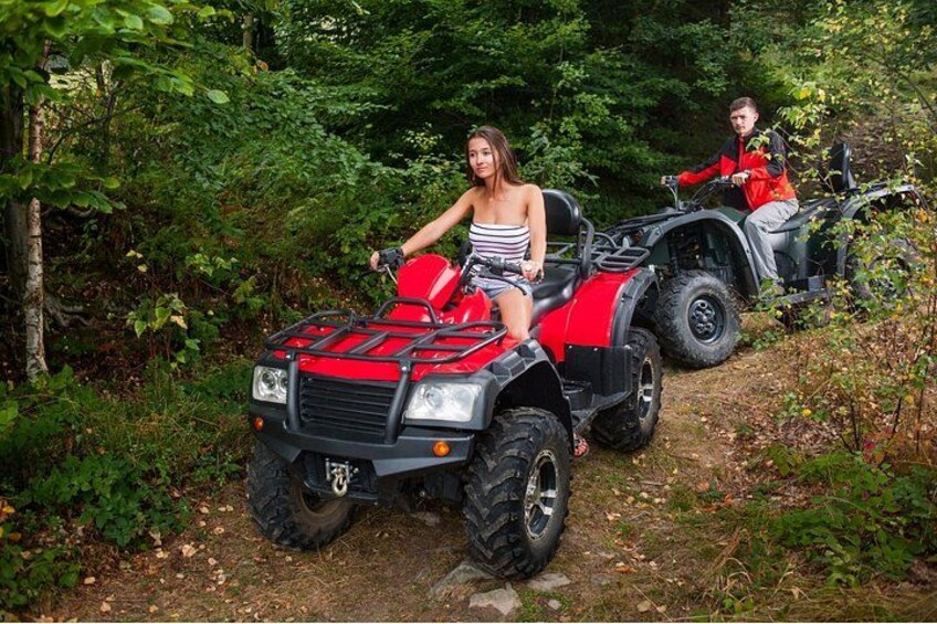 Two people on red all-terrain vehicles in a forested area. 2