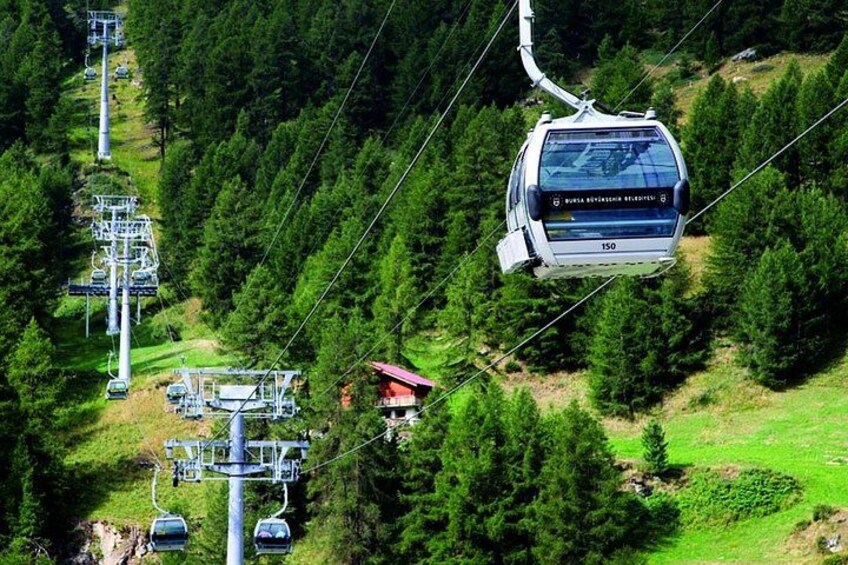 A cable car system with a chairlift suspended between two towers, surrounded by dense forest. 2
