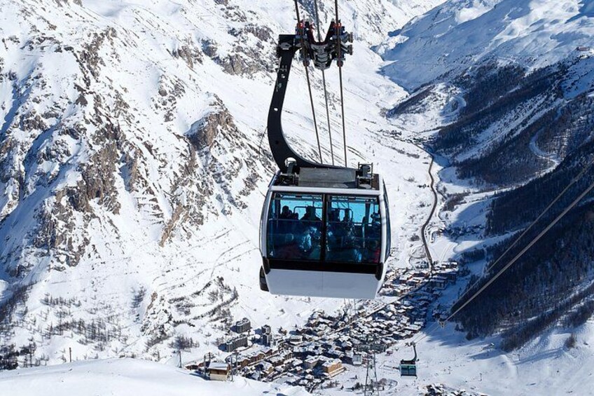 A cable car suspended over a snowy mountain landscape with a village below. 1