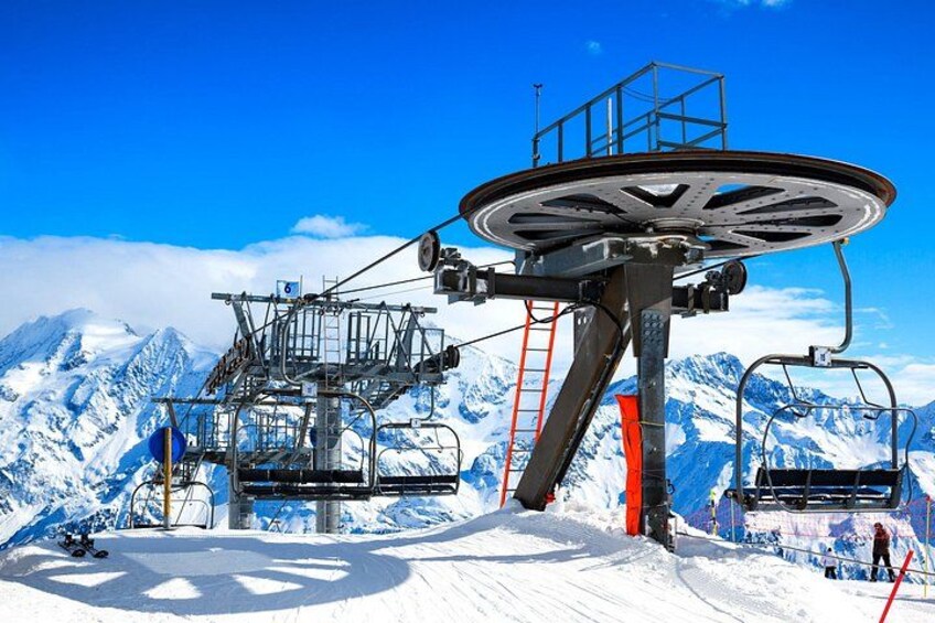 A ski lift with chairs and a control tower against a snowy mountain backdrop. 4