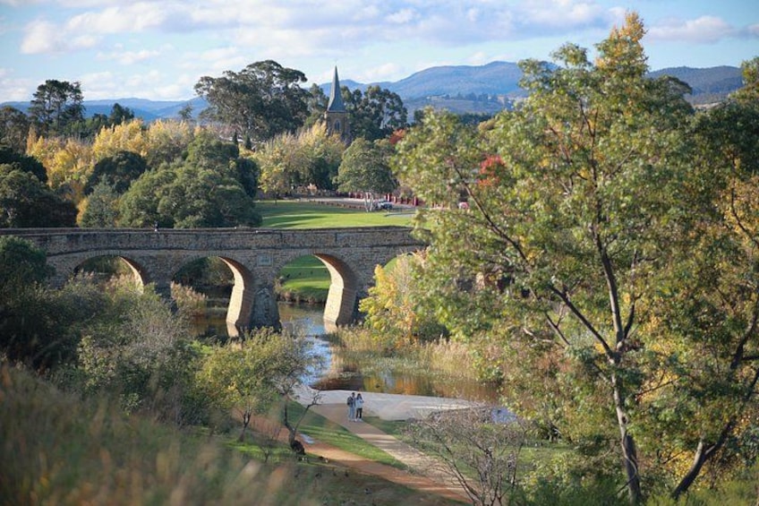 A stone bridge over a river, surrounded by trees and a distant church. 3