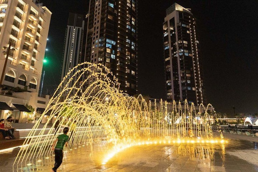 A nighttime cityscape with illuminated water fountains and tall buildings. 5