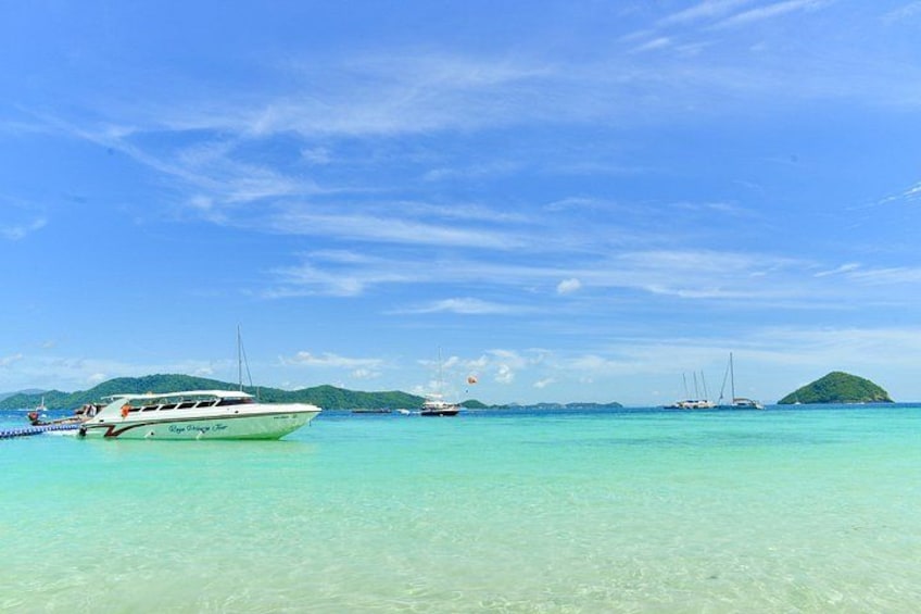 A clear turquoise sea with boats and a small island in the distance. 3