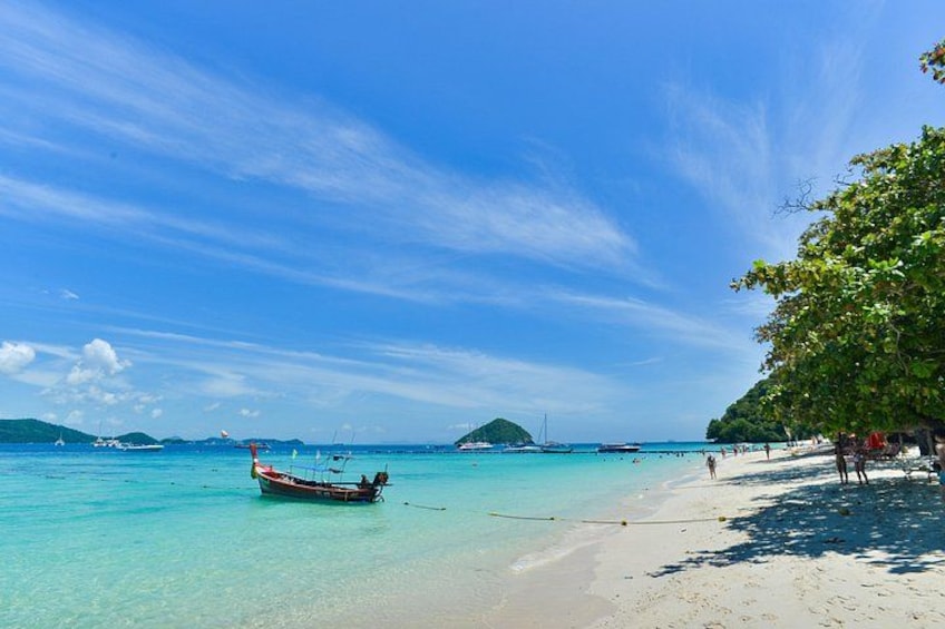 A beach with clear turquoise water, a boat, and a sandy shore with people. 5
