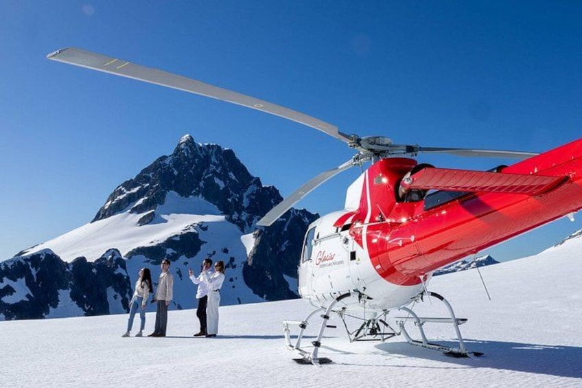 A red and white helicopter on snow with a mountain in the background. 2