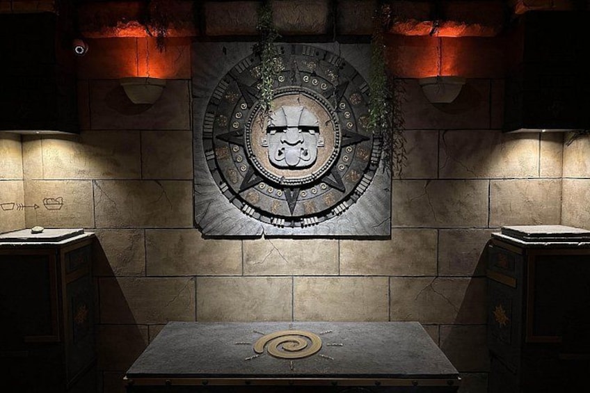 Un mur en pierre orné d’un emblème circulaire, deux armoires et une table au motif en spirale. 1