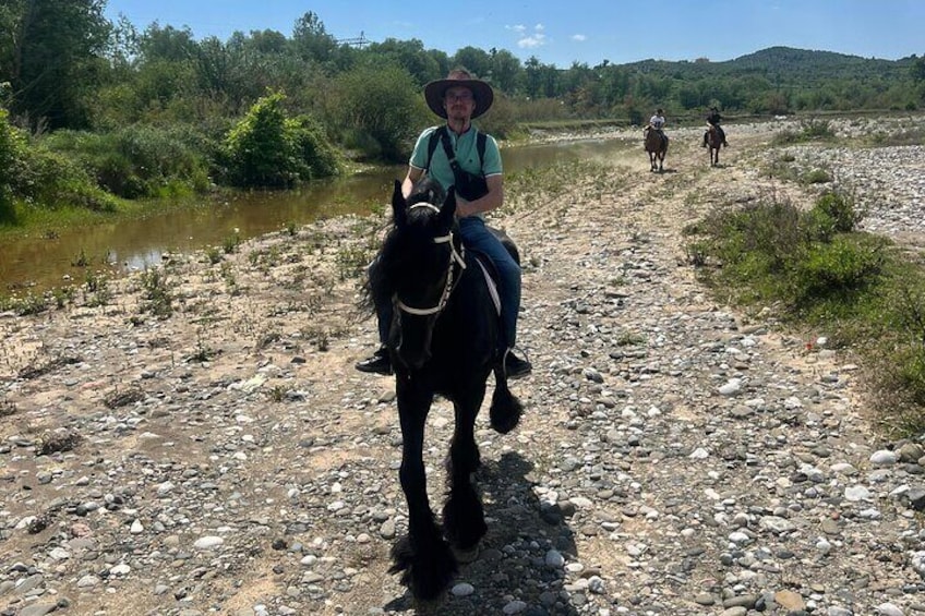 Une personne à cheval, sur un sentier rocailleux, avec une rivière d’un côté et des collines en arrière-plan. 3