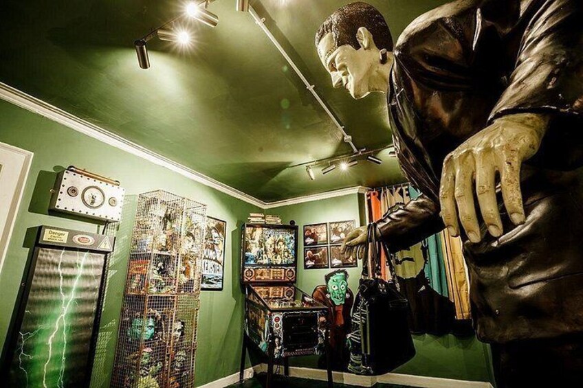 A room with green walls, a mannequin, and various items including a cage, a box, and a poster. 5