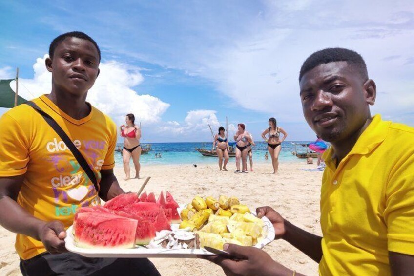 Deux personnes sur une plage, devant une assiette de tranches de pastèque et d’ananas. 5