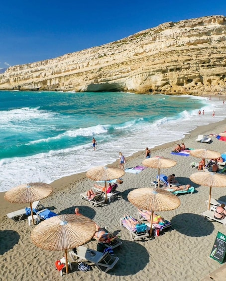 Een strand met mensen die zonnebaden onder rieten parasols, de oceaan en rotsachtige kliffen. 5