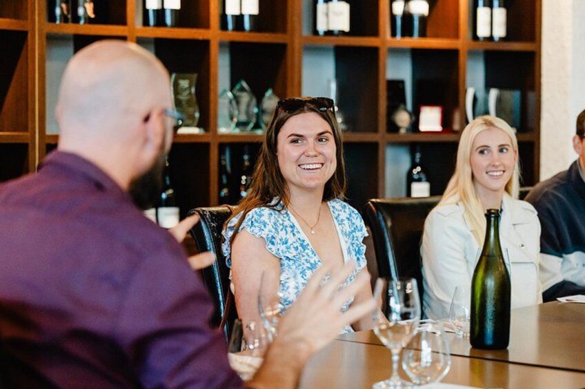 A group of people sitting at a table with wine bottles and glasses. 3