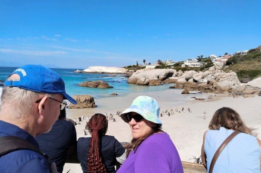 Eine Gruppe von Menschen am Strand, mit blauem Himmel und Felsformationen im Hintergrund. 4