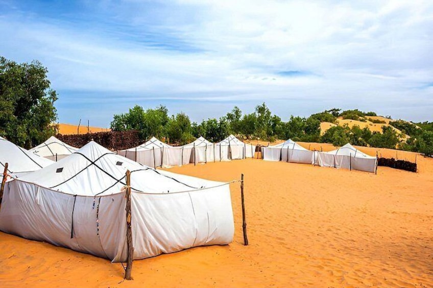 A desert campsite with white tents and sparse vegetation. 2
