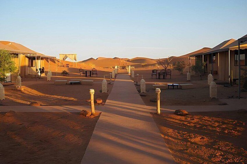 A desert resort with tents and buildings, a paved walkway, and sand dunes in the background. 3