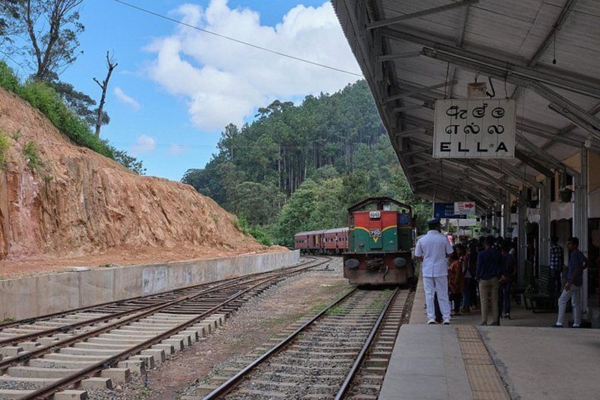 A train station with a platform, a train on the tracks, and a sign with text. 1