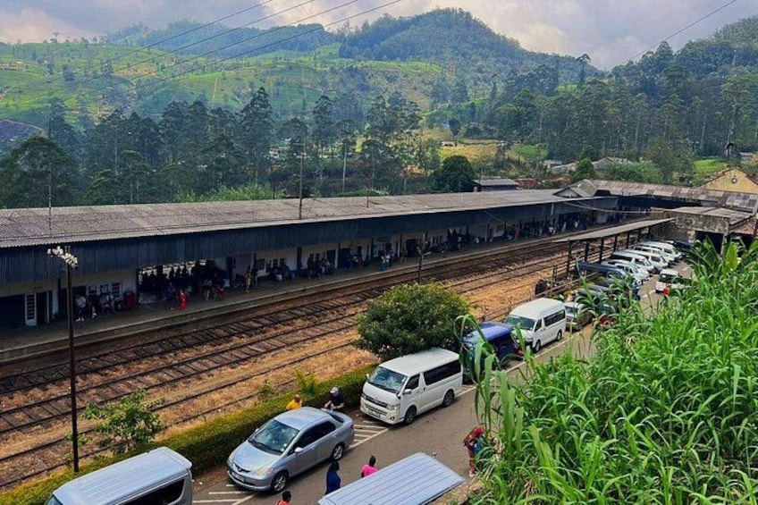 A train station with tracks, a covered waiting area, and parked cars. 4