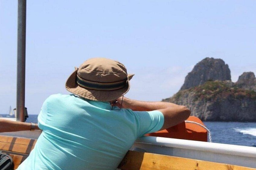 Una persona con un cappello e una camicia blu che guarda il mare, con una costa rocciosa sullo sfondo. 5