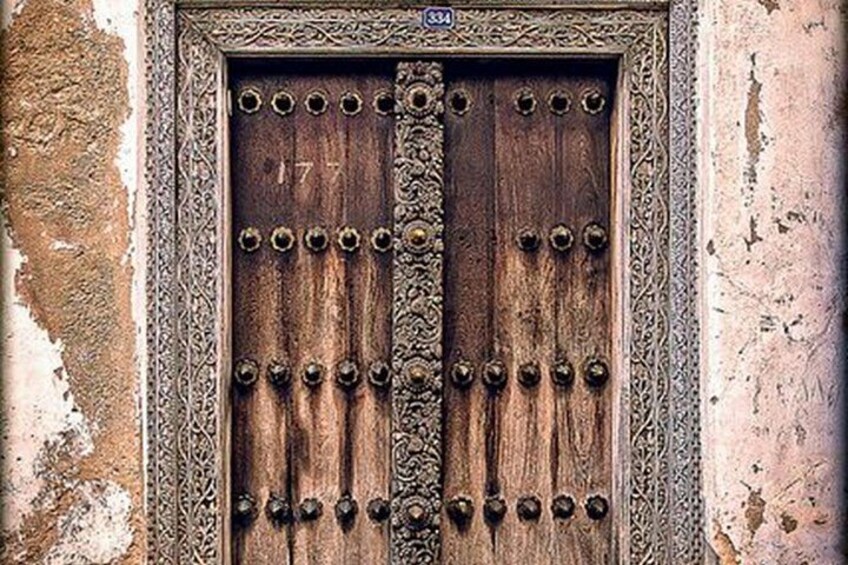 A wooden door with metal studs, a central handle, and a number '177' on the upper left. 4
