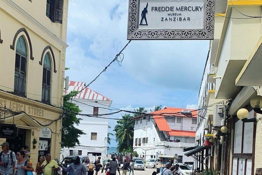 A busy street with a museum sign, shops, and pedestrians. 3