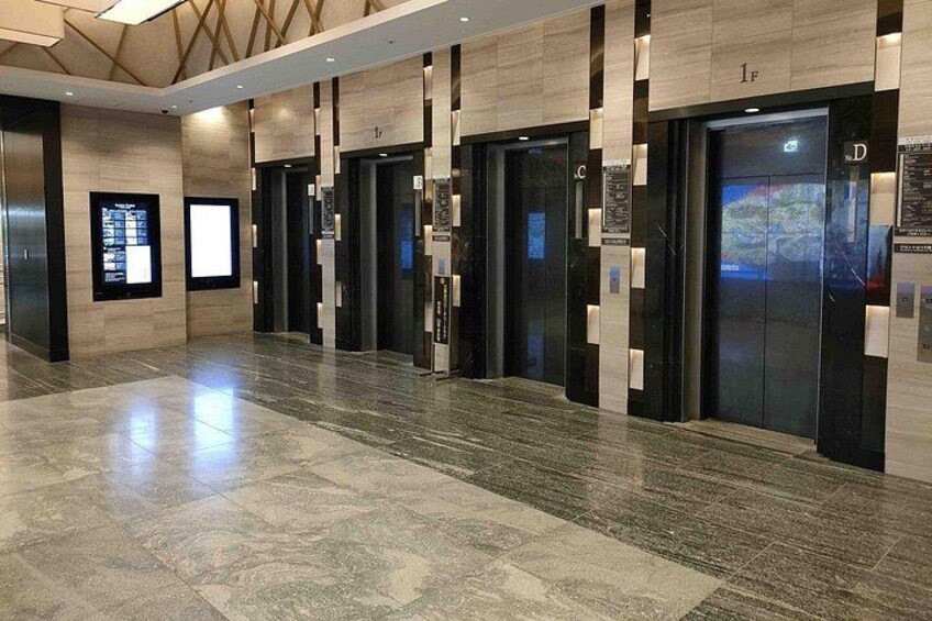 A modern elevator lobby with multiple elevators, polished marble flooring, and digital displays on the walls. 4