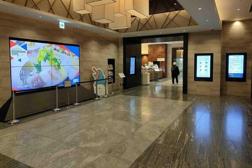 A spacious lobby with a large digital display, a reception desk, and informational signs. 3