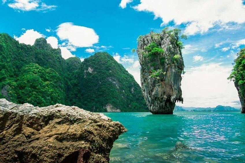A limestone karst formation surrounded by clear turquoise water and lush green cliffs. 3