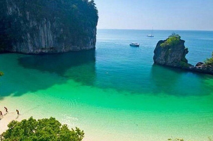 A coastal landscape with clear turquoise water, a sandy beach, and rocky formations. 4