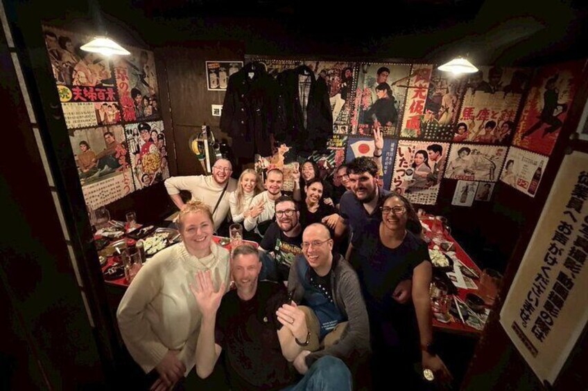 Un grupo de personas en una habitación con carteles en las paredes y diversos objetos en estantes. 5