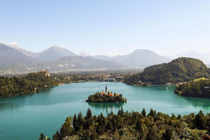 Un lac entouré de montagnes, une petite île avec une église et, au loin, un château. 1