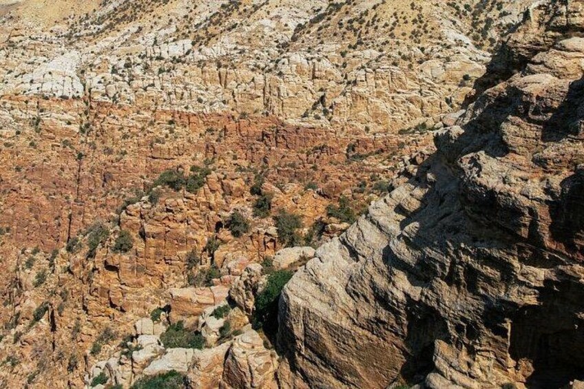 A rugged canyon landscape with layered rock formations and sparse vegetation. 2