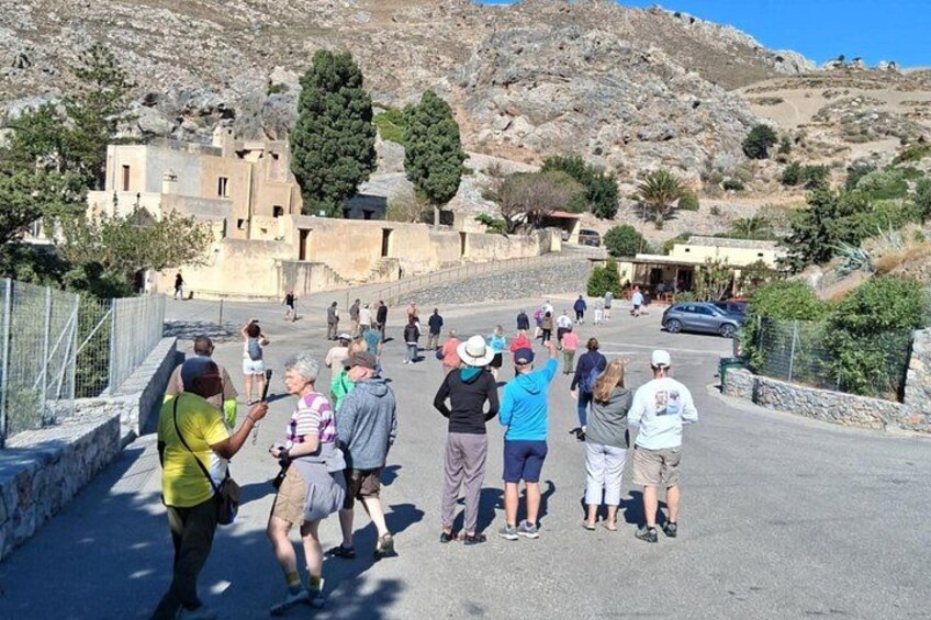 A group of people walking on a paved path in a hilly area with buildings and trees in the background. 5