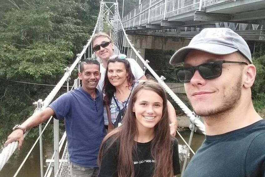 Un groupe de personnes se trouve sur un pont suspendu, doté de garde-corps et de câbles métalliques, et est entouré de verdure. 4