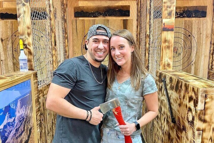 Two people holding axes in a wooden cabin with a target on the wall. 2