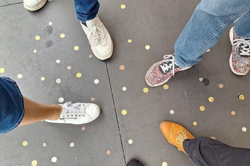 A person's feet wearing different types of shoes on a floor with scattered coins. 4