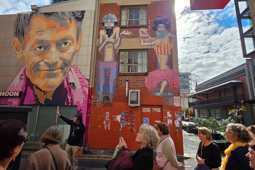 Une fresque murale orne un bâtiment, et des personnes l’observent. 3
