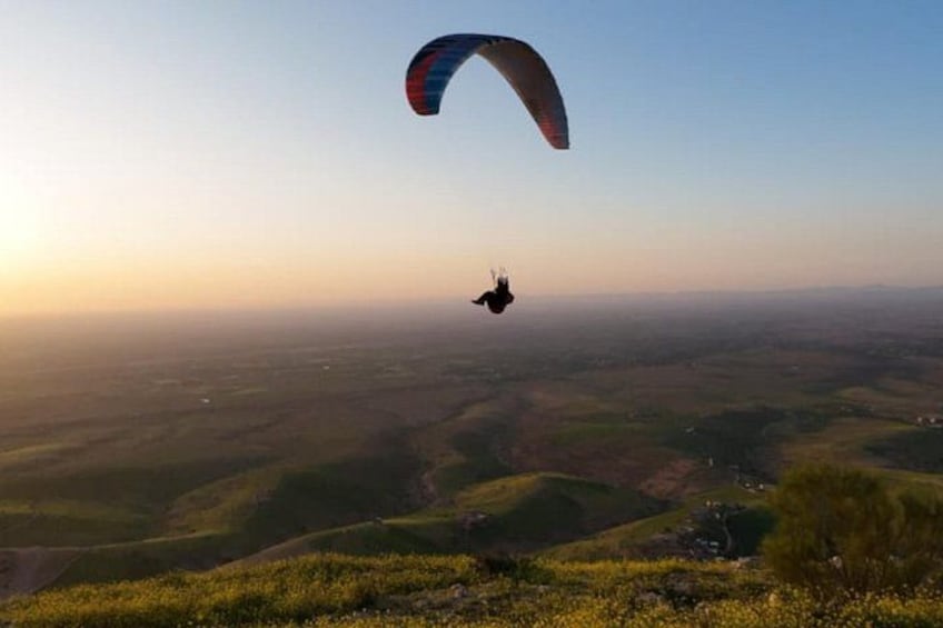 Una persona pratica paracadutismo in parapendio sopra un paesaggio collinare al tramonto. 1