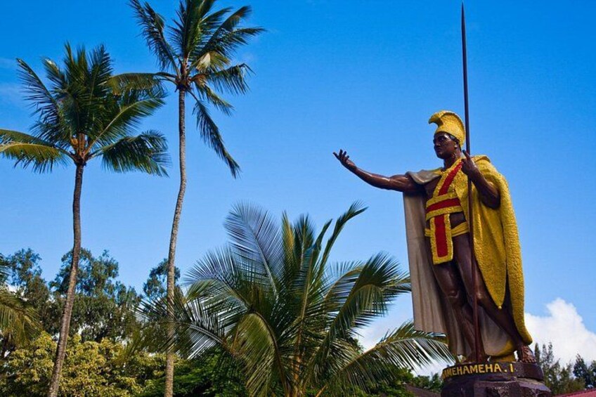 A statue of a figure with a spear, wearing a yellow and red garment, set against a backdrop of palm trees and a clear blue sky. 2