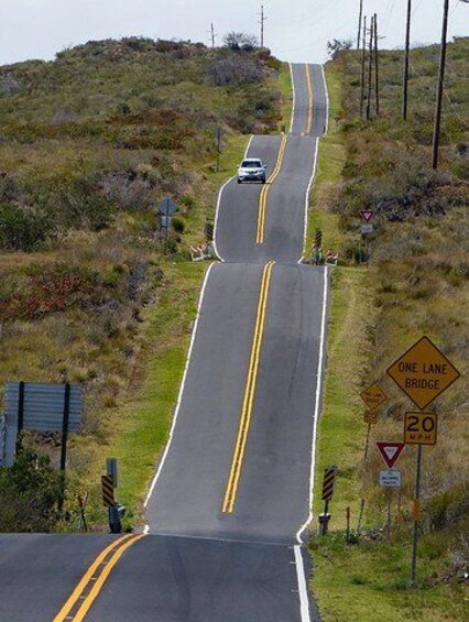 A winding road with a one-lane bridge ahead, surrounded by hills and vegetation. 4