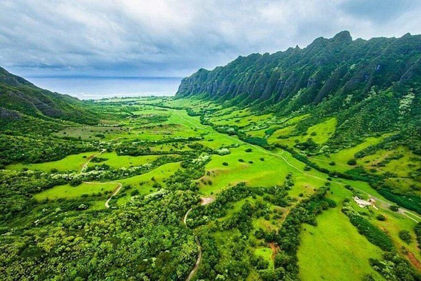A lush valley with winding paths, dense greenery, and a mountain range in the background. 5