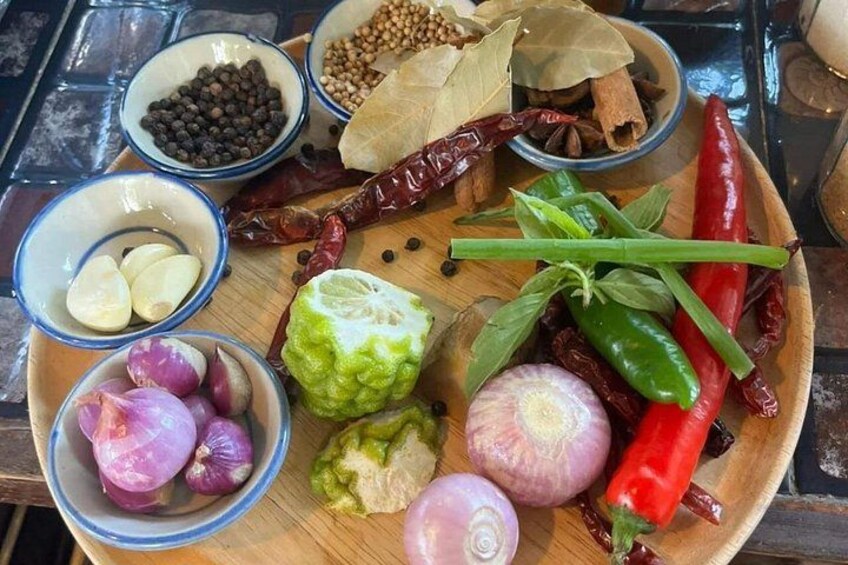 A wooden cutting board with various spices and herbs, including red chili peppers, green chilies, and onions. 3