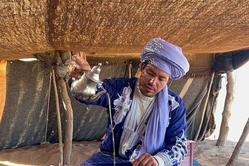 A person pouring a liquid from a metal container under a thatched roof. 3