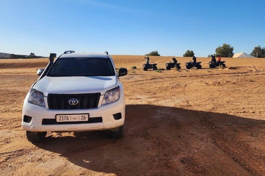 A white SUV parked on a sandy terrain with four off-road vehicles in the background. 1