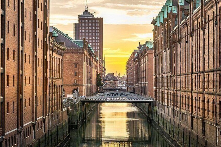 A canal with buildings on either side, a bridge in the center, and a sunset in the background. 3