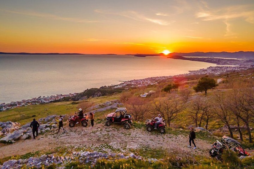 A sunset over a coastal landscape with people and ATVs. 5